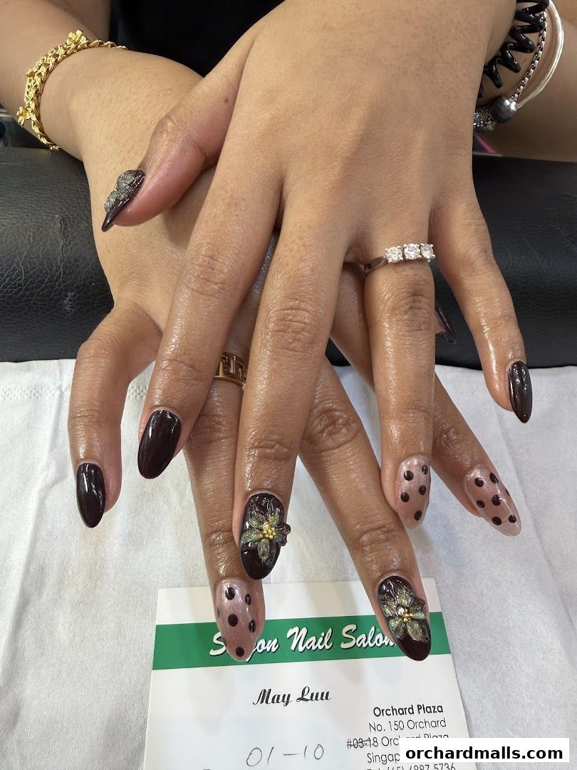 Close-up of hands with intricate nail art, featuring dark polish, polka dots, and floral embellishments.