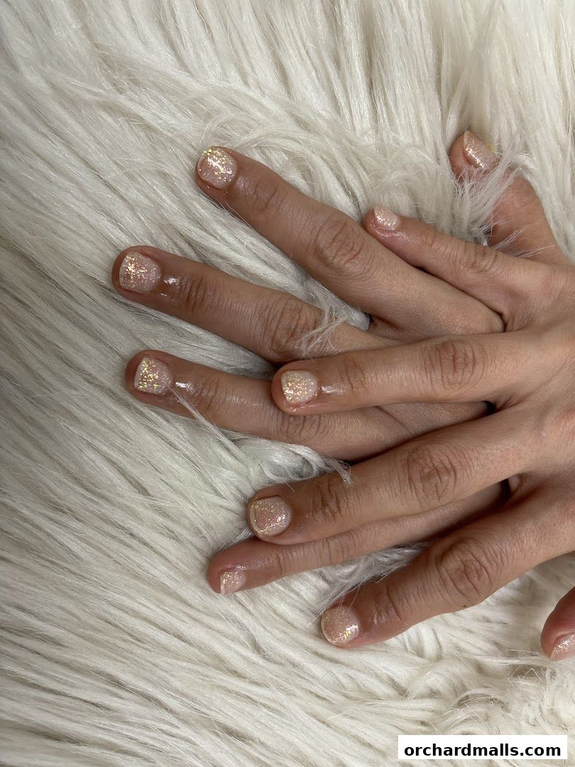 Close-up of hands with sparkling, glittery nail polish on a fluffy white surface.