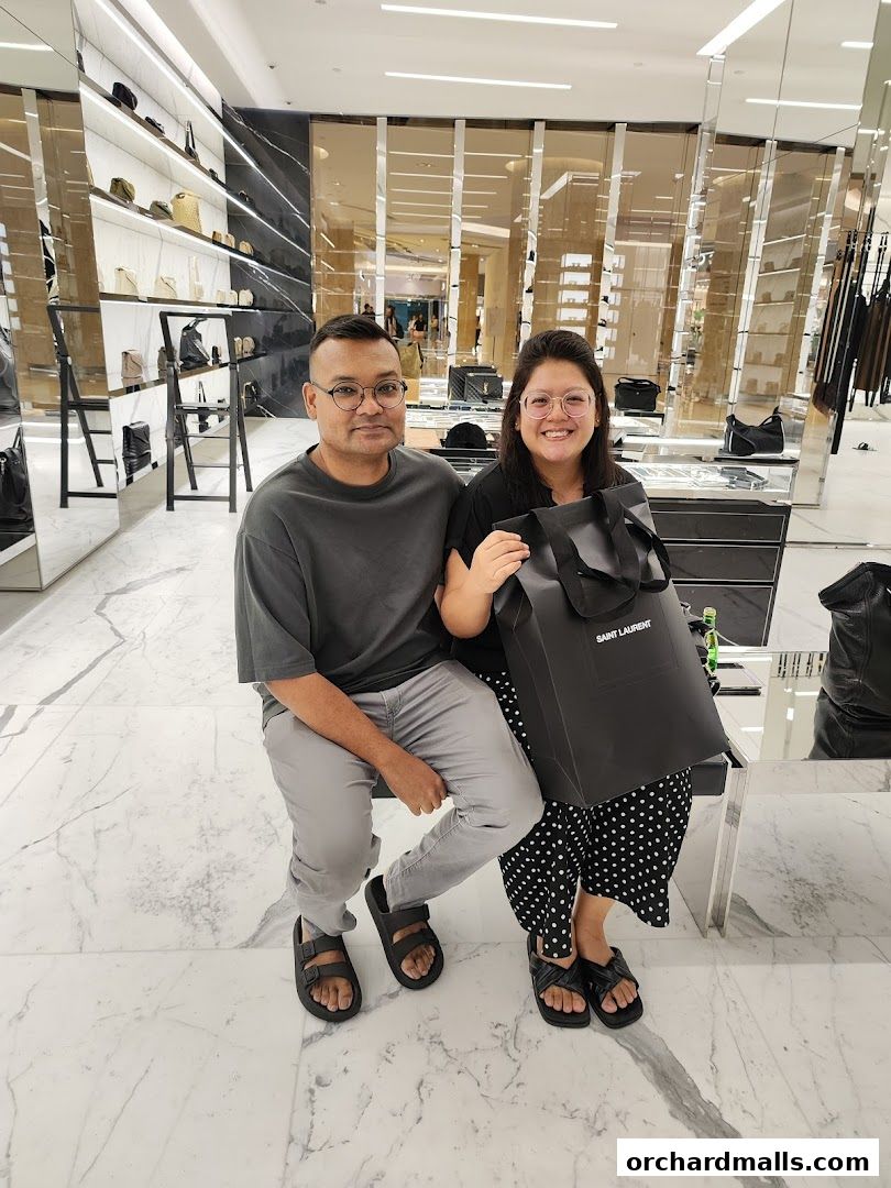 A couple poses with a Saint Laurent shopping bag inside a luxury boutique.