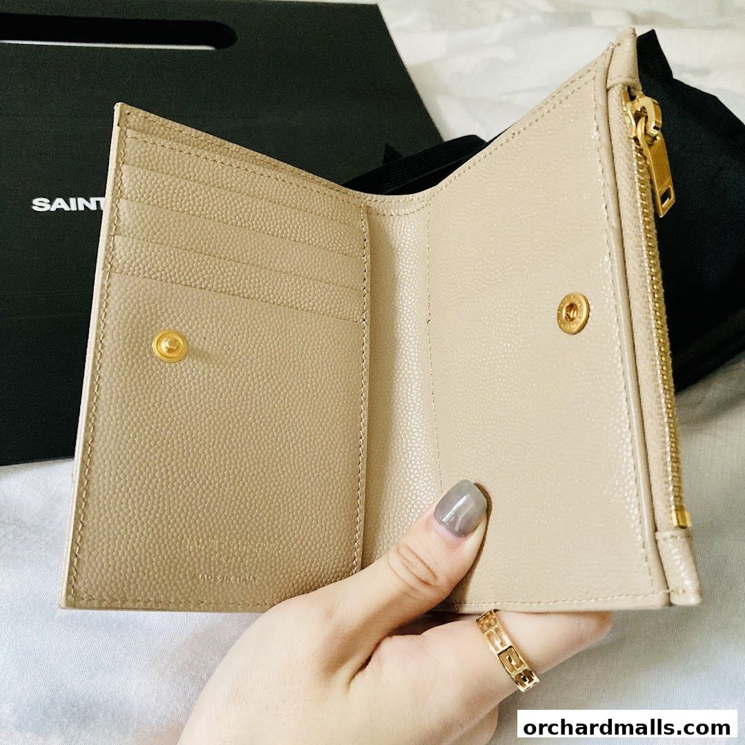 A hand holds open a beige Saint Laurent wallet, revealing card slots and a zippered compartment.