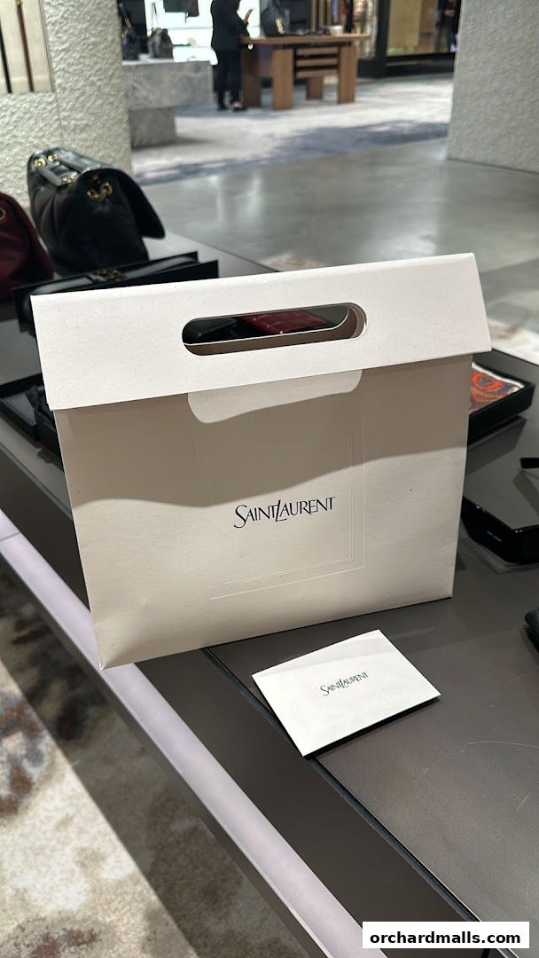 A Saint Laurent shopping bag and a small card on a display table inside a store.