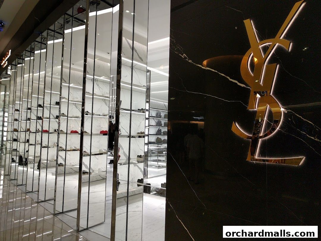 The Saint Laurent shop features a striking gold logo on a black marble wall and a display of shoes on mirrored shelves.