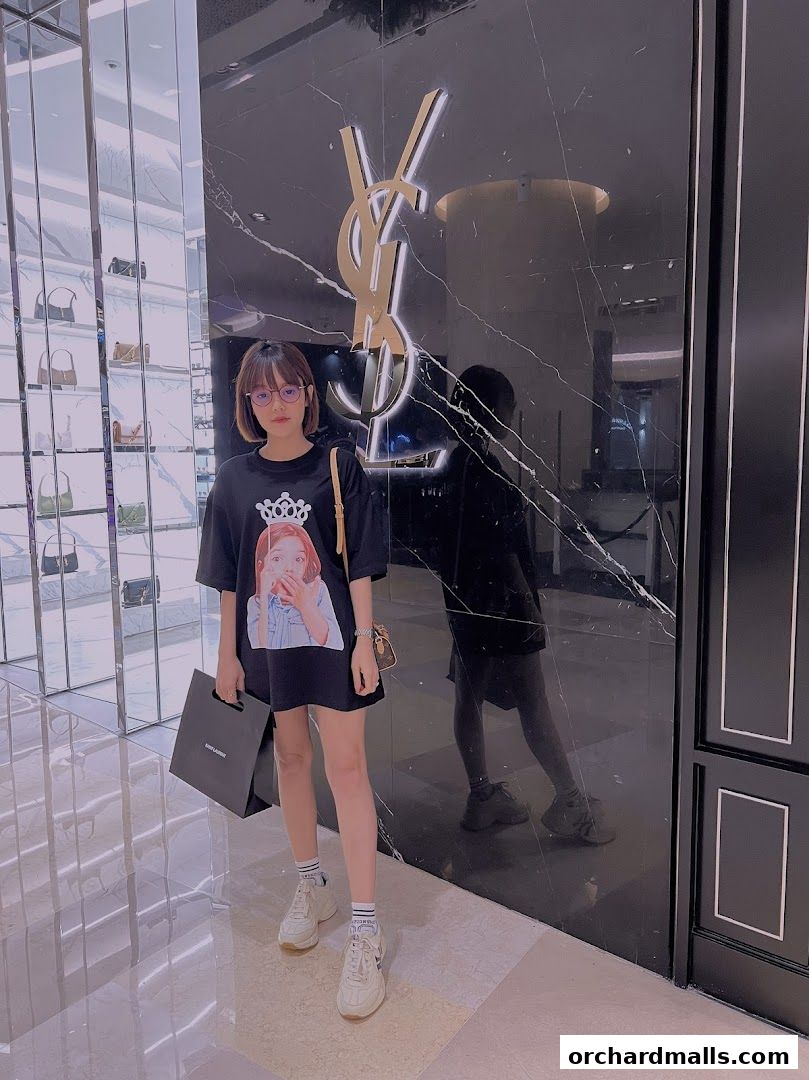 A woman stands in front of a Saint Laurent store with the iconic YSL logo.