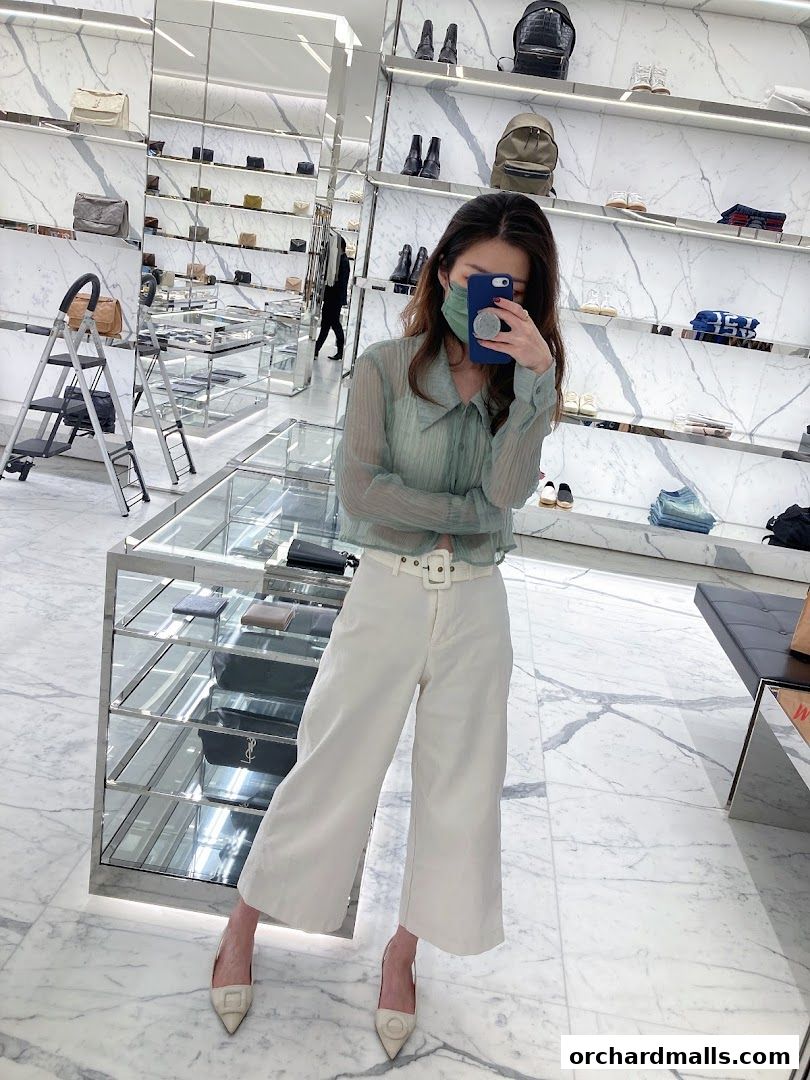 A woman takes a selfie in a well-lit luxury boutique, showcasing fashion items.