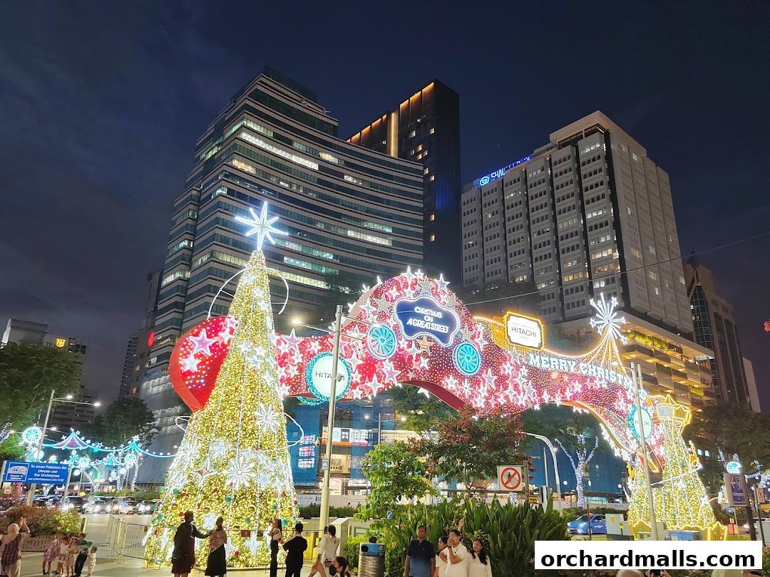 A festive Christmas street scene with a large decorated tree and archway at night.
