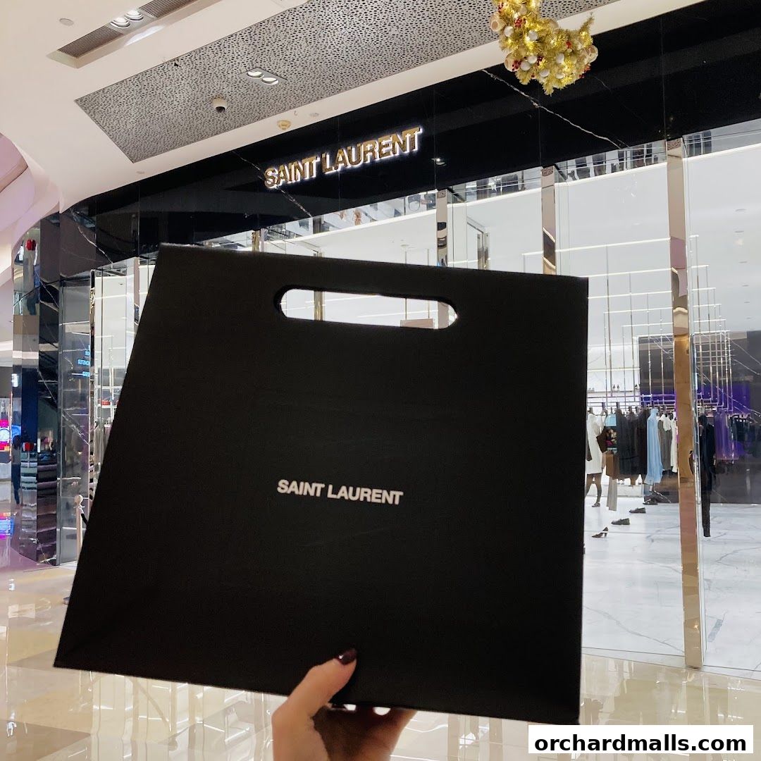 A black Saint Laurent shopping bag is held in front of the store's entrance.