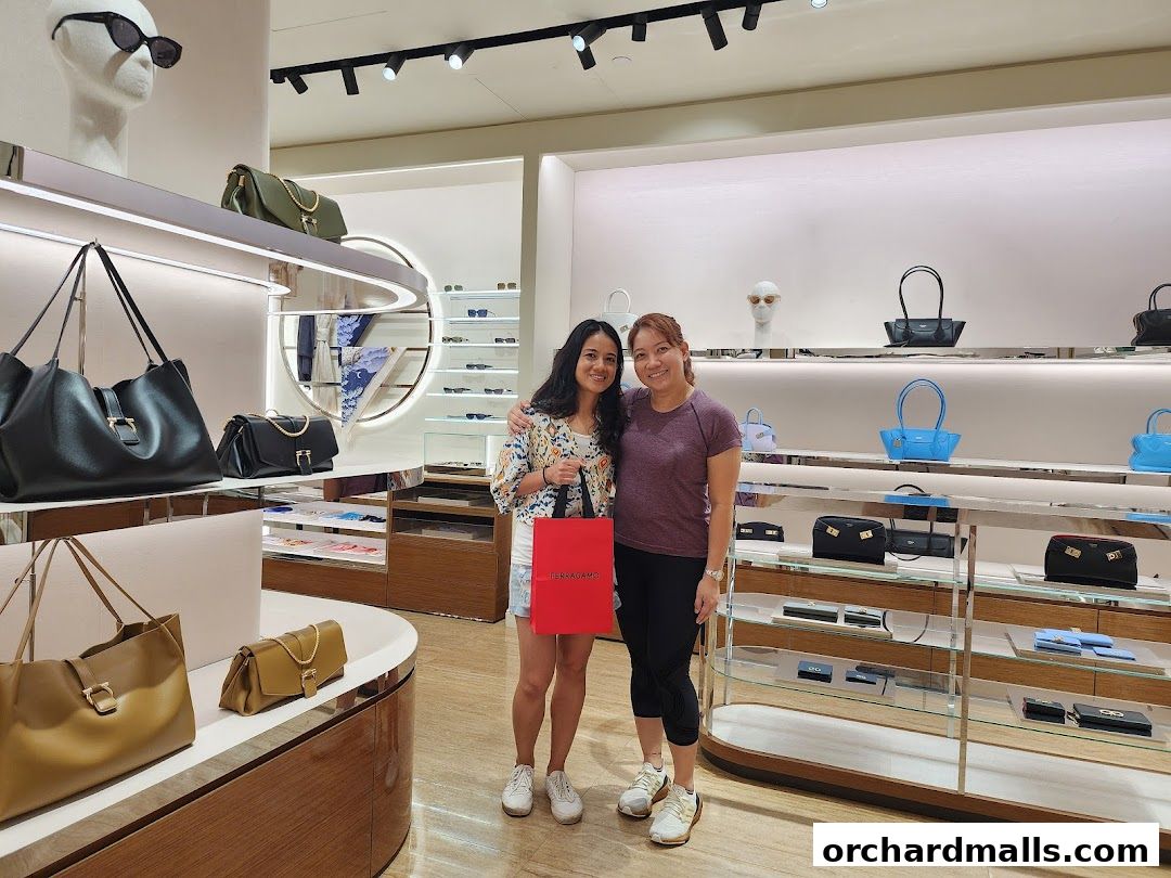 Two women smiling inside a Salvatore Ferragamo store with handbags on display.