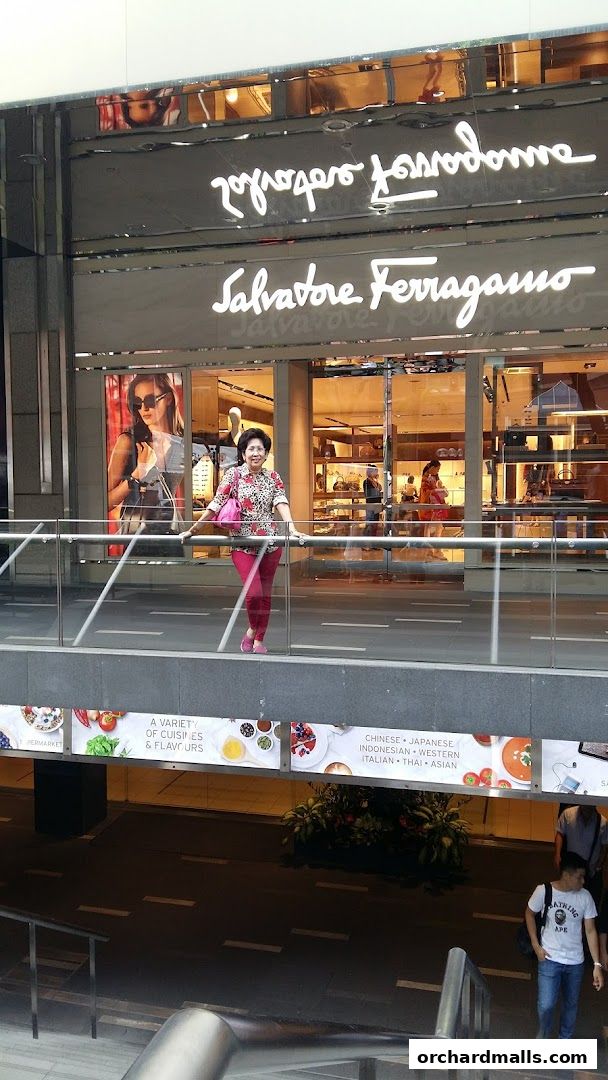 A woman poses in front of the Salvatore Ferragamo store entrance with a large advertisement.