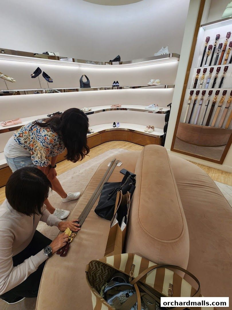 Two women examine belts and shoes in a well-lit Salvatore Ferragamo store.