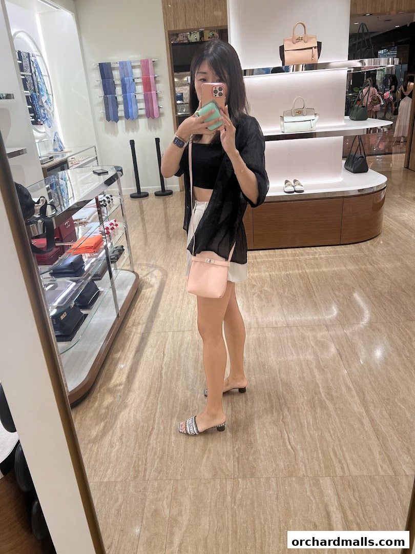 A woman takes a mirror selfie in a Salvatore Ferragamo store, showcasing handbags and accessories.