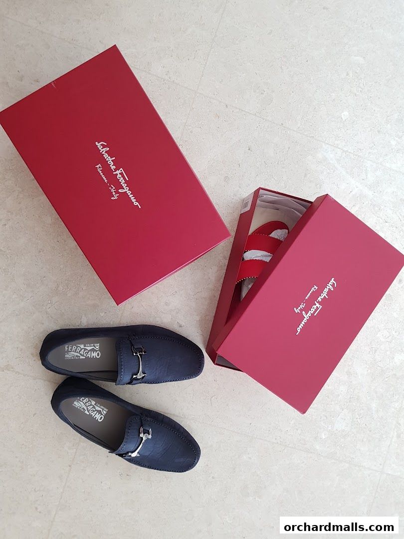 A pair of navy blue Salvatore Ferragamo loafers and red sandals in their signature red boxes.