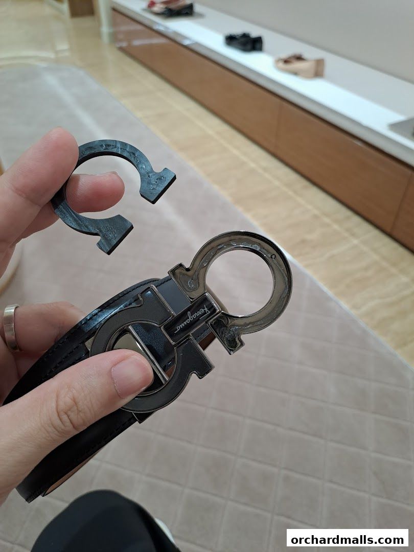 A hand holds a black Salvatore Ferragamo belt with a signature Gancini buckle.