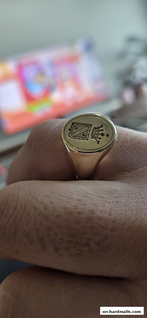 A close-up shot of a gold signet ring with an engraved crest and crown.