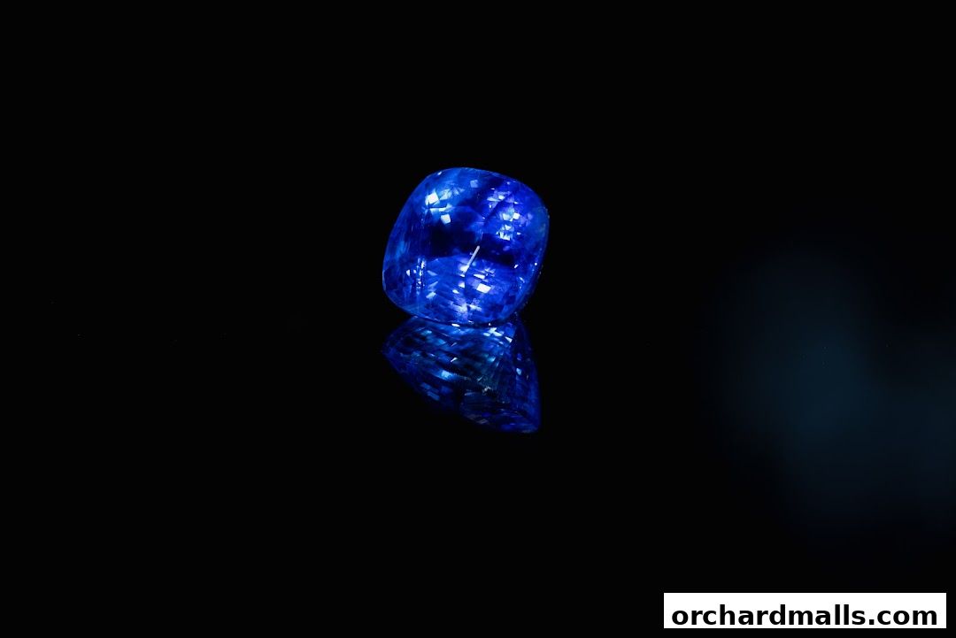 A stunning, faceted blue sapphire gemstone displayed on a reflective black surface.