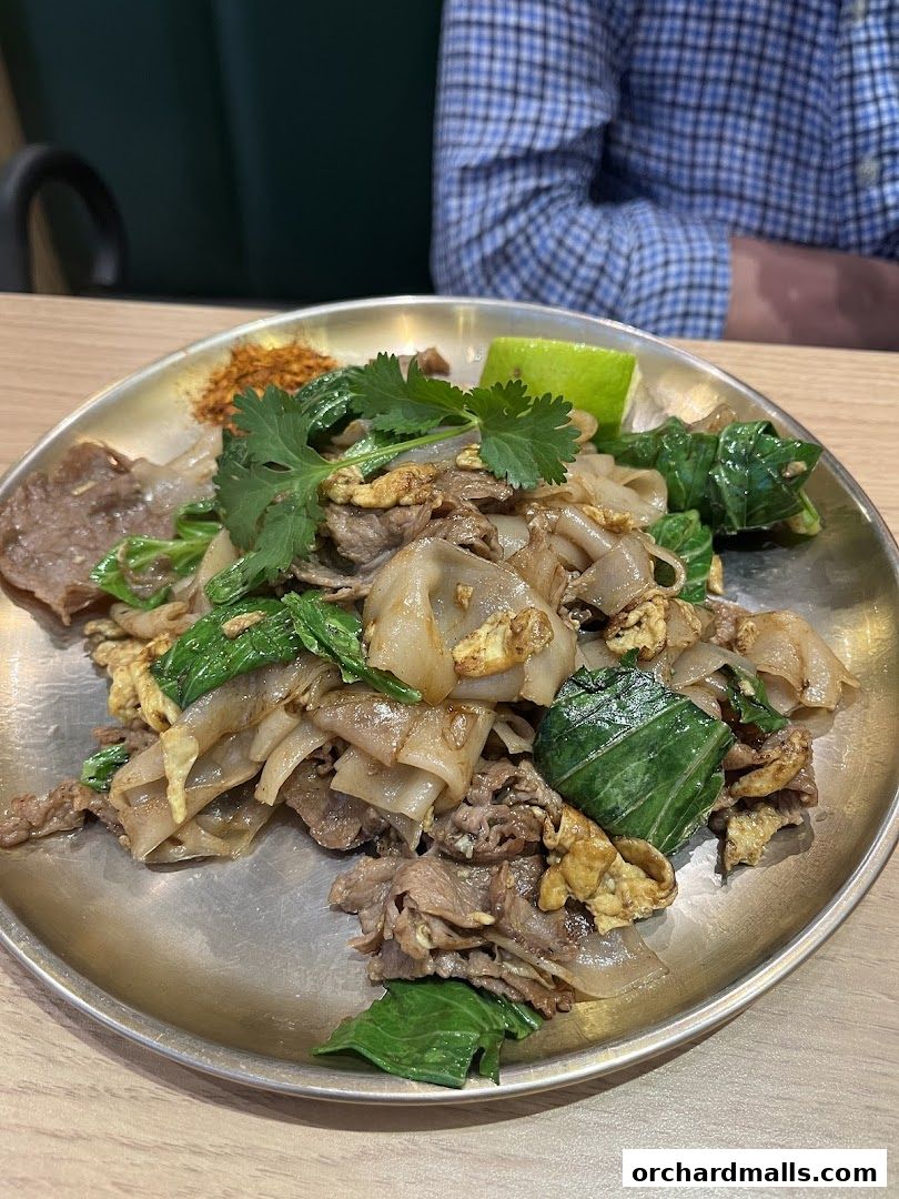 A plate of Pad See Ew with beef, vegetables, and a lime wedge.