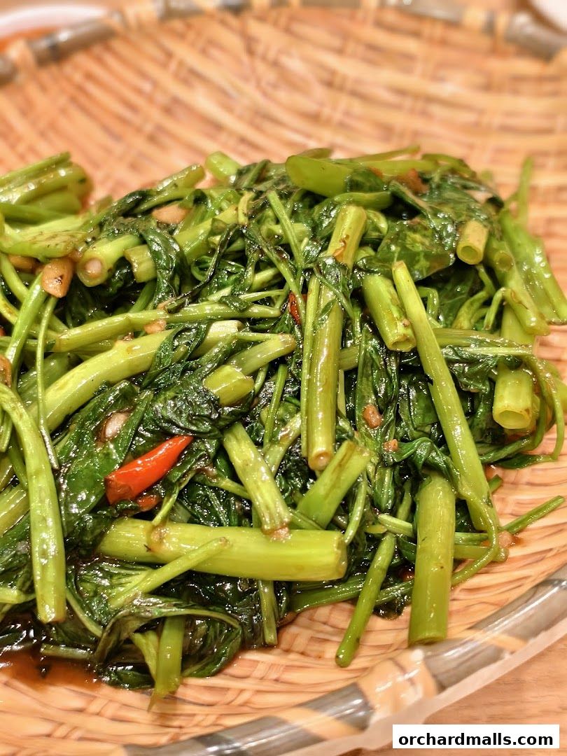 A close-up shot of stir-fried water spinach with chili and garlic, served on a woven platter.