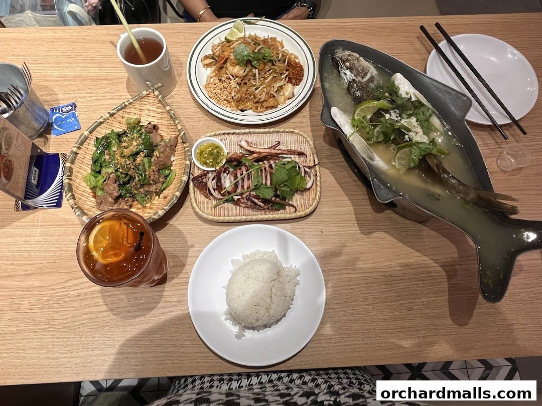 A table laden with delicious Thai dishes including Pad Thai, grilled squid, beef with vegetables, and a whole steamed fish.