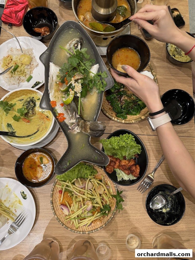 A table laden with various Thai dishes, including a whole steamed fish, curry, and mango salad.