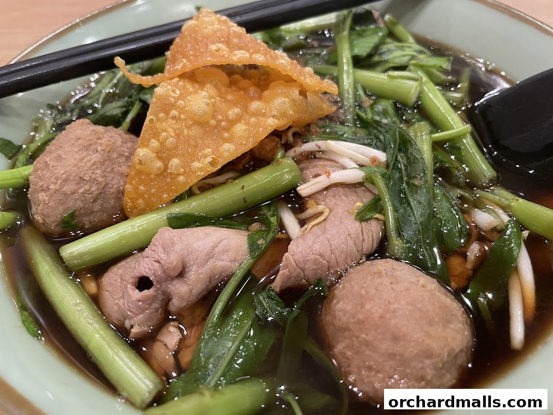 A close-up shot of a delicious bowl of Thai noodle soup with meatballs and vegetables.