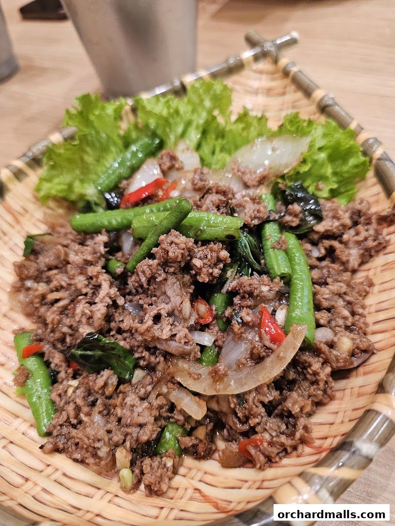 A close-up of a Thai minced beef dish with long beans and chili, served on a woven platter.