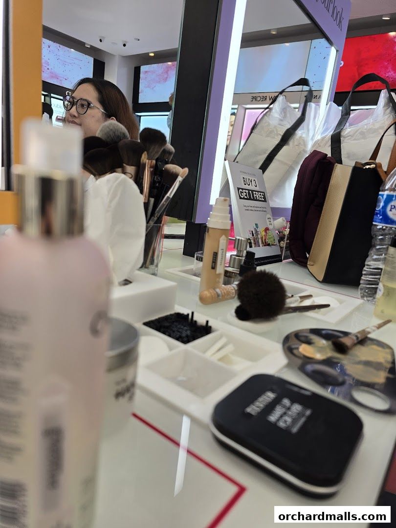 A woman is reflected in a mirror at a makeup counter with various beauty products and brushes.