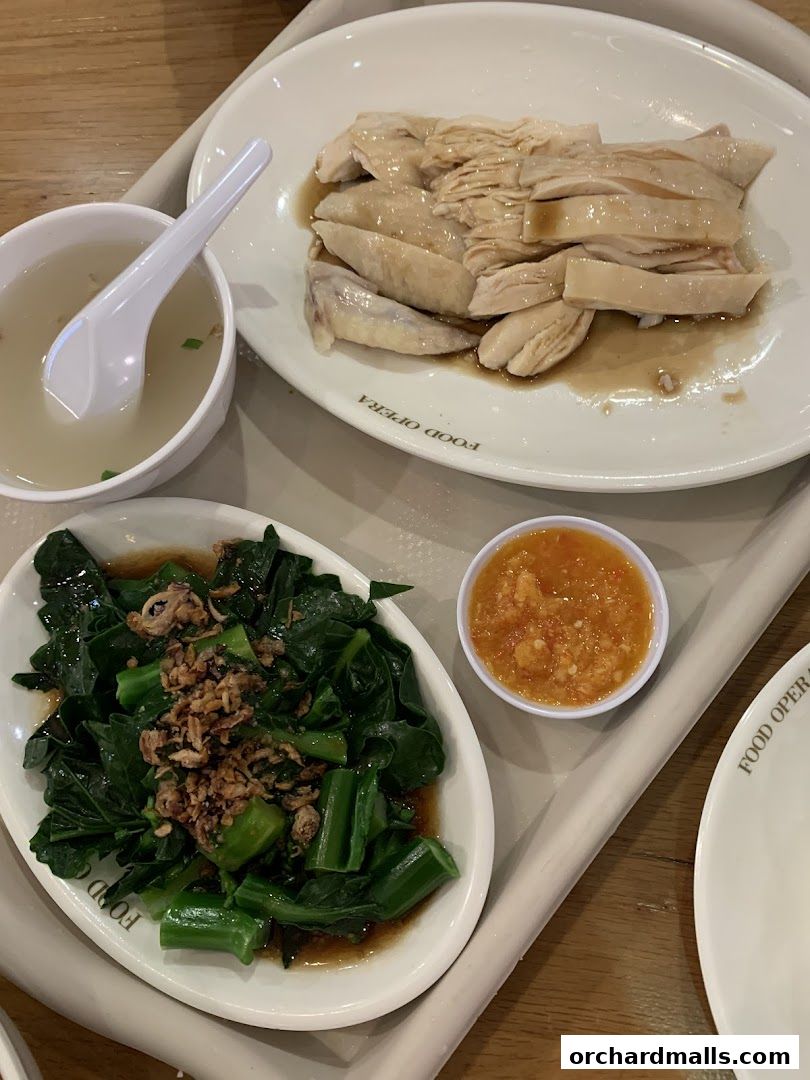A plate of Hainanese chicken rice with a side of stir-fried vegetables and soup.