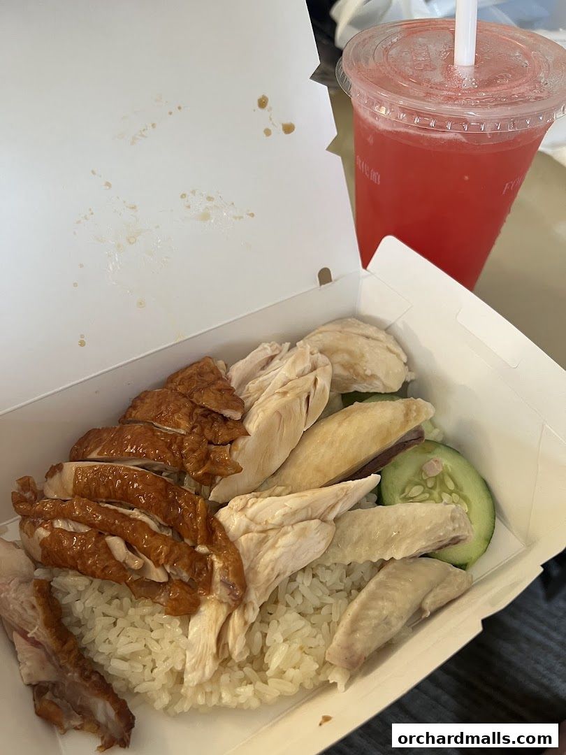 A takeaway box filled with Hainanese chicken rice and a red beverage.
