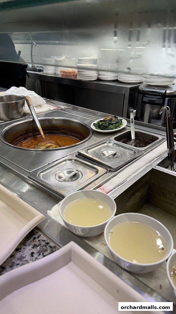 A close-up of a food service counter with steaming pots of soup and side dishes.