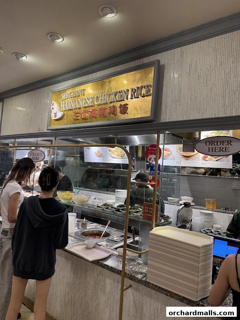 Customers ordering Hainanese Chicken Rice at a food stall with a prominent sign.