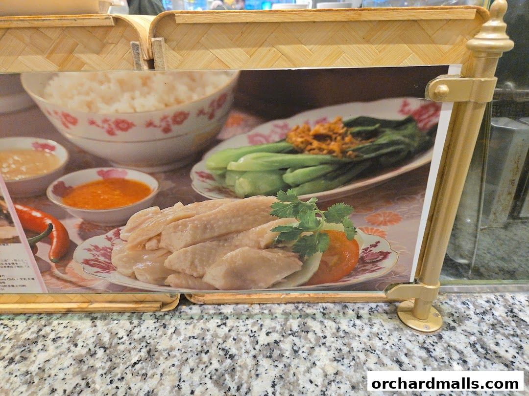 A close-up of a Hainanese chicken rice dish with rice, chicken, vegetables, and sauces.