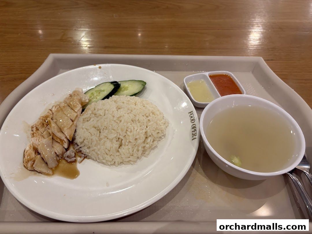 A plate of Hainanese chicken rice with soup and condiments on a tray.