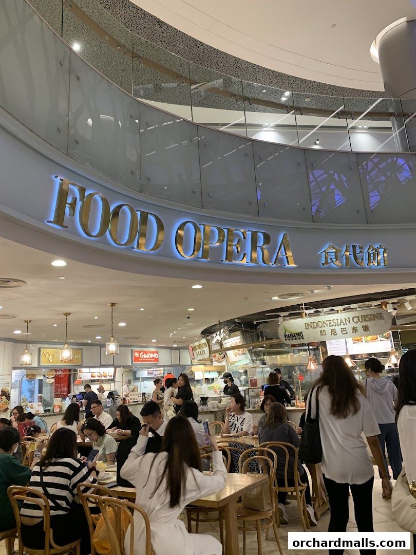 A busy food court with many diners seated at tables and various food stalls visible.