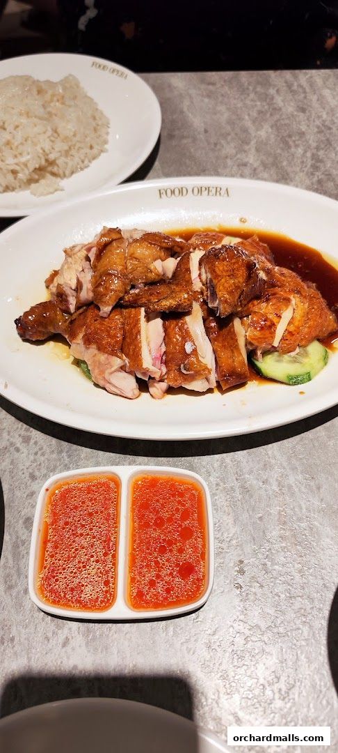 A plate of delicious Hainanese chicken rice with chili sauce and a side of rice.