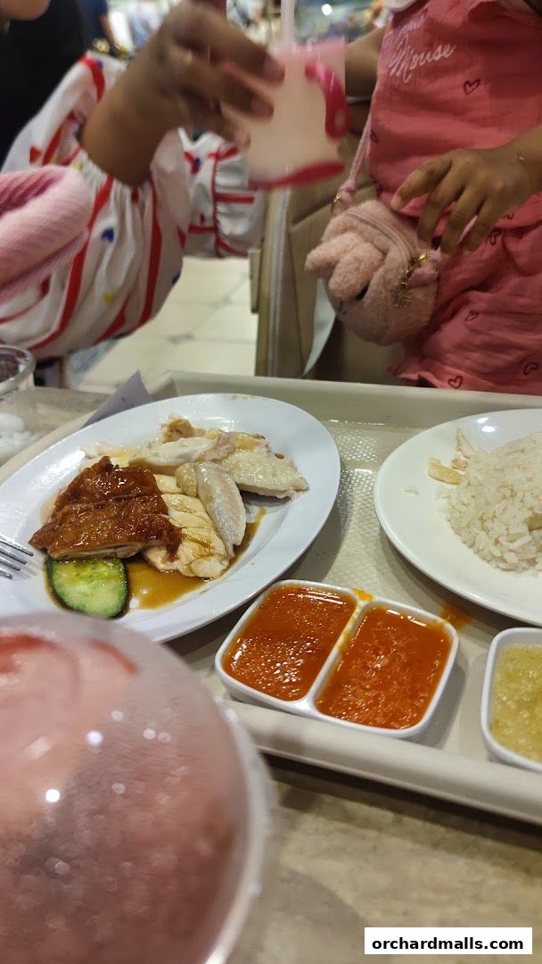 A close-up of Hainanese chicken rice with dipping sauces and drinks.