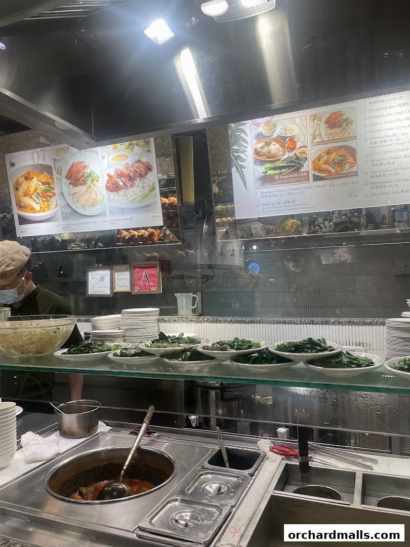 A display of Hainanese chicken rice dishes and other menu items at a restaurant counter.
