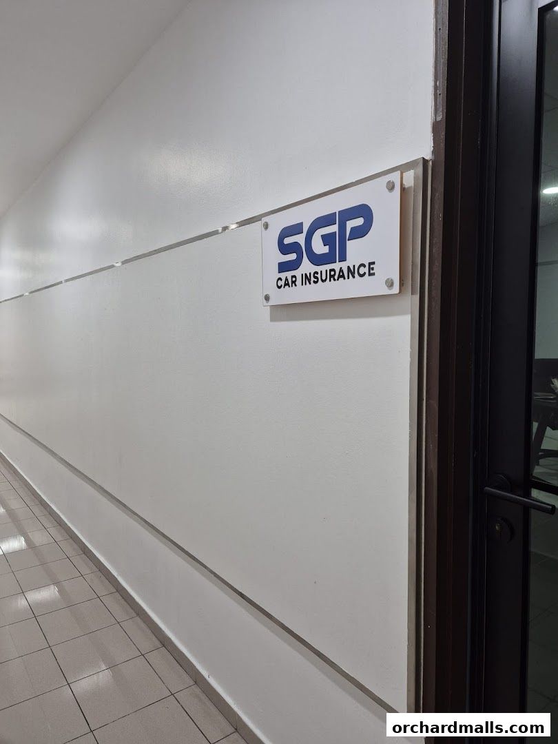 A sign for SGP Car Insurance is mounted on a white wall next to a dark door.