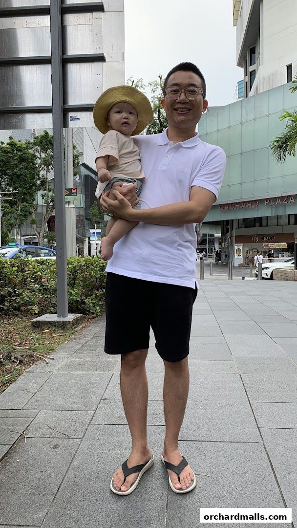 A man holds a baby wearing a hat outside Orchard Plaza.