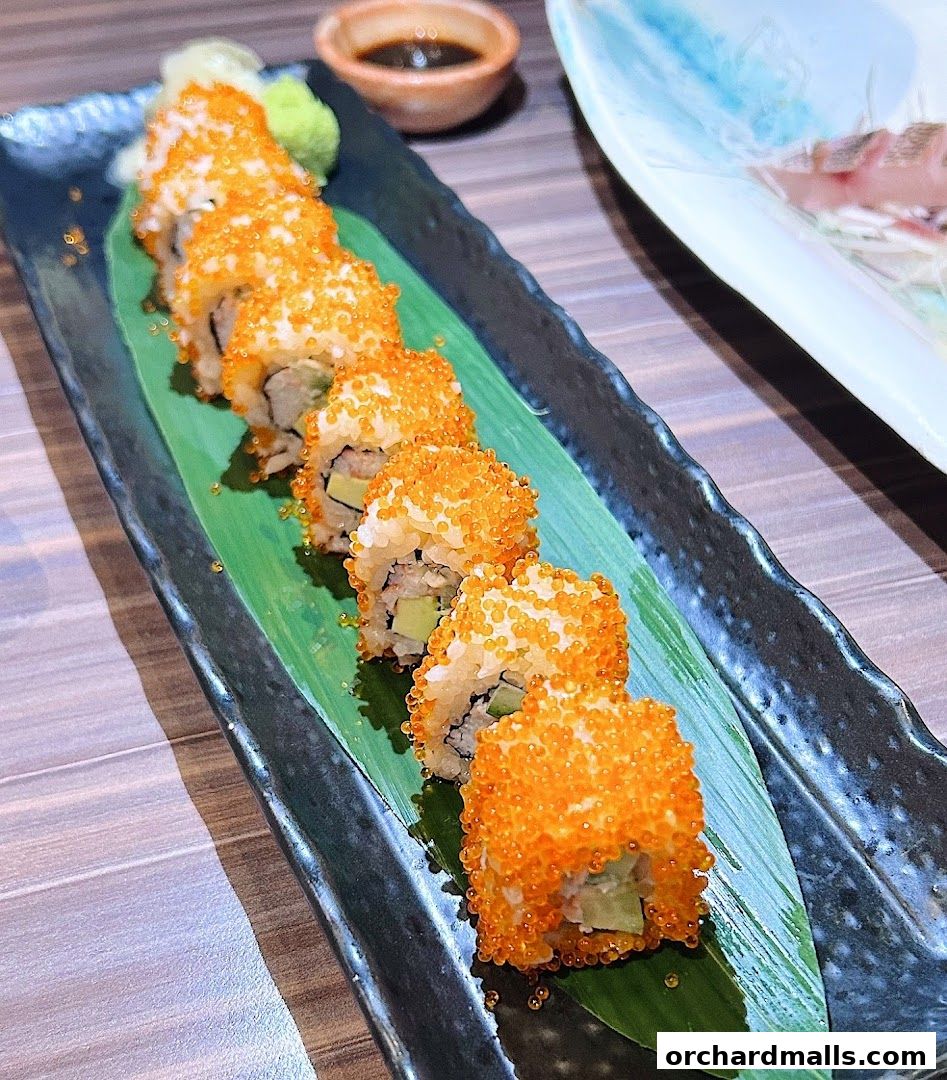 A close-up of California rolls with orange roe, served on a banana leaf with soy sauce.