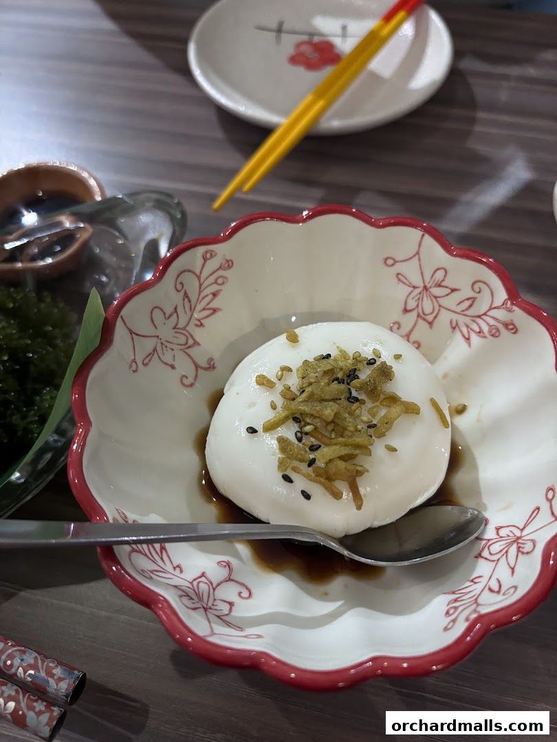 A close-up of a white dessert with toppings in a decorative bowl with a spoon.