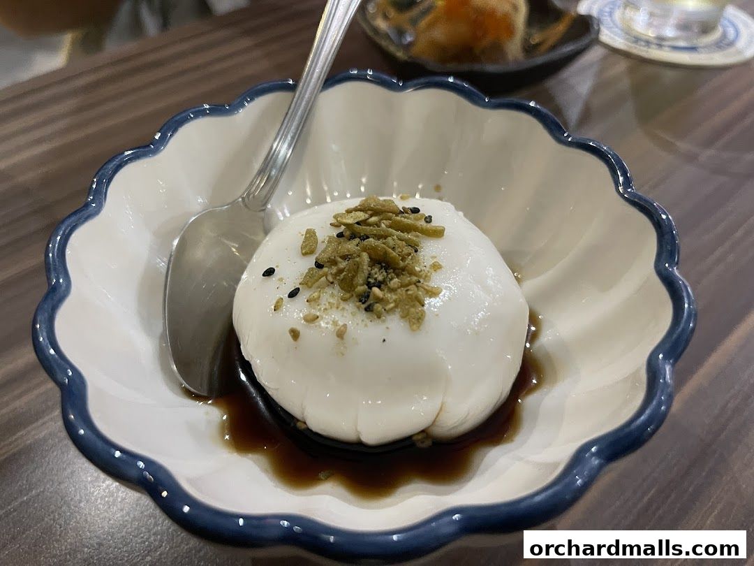 A delicate dessert with white pudding, topped with green flakes and black sesame seeds.