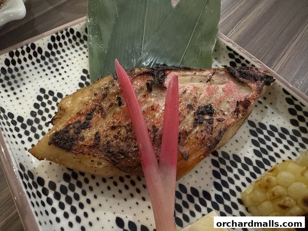 A close-up of a grilled fish dish with pickled ginger and corn on a decorative plate.