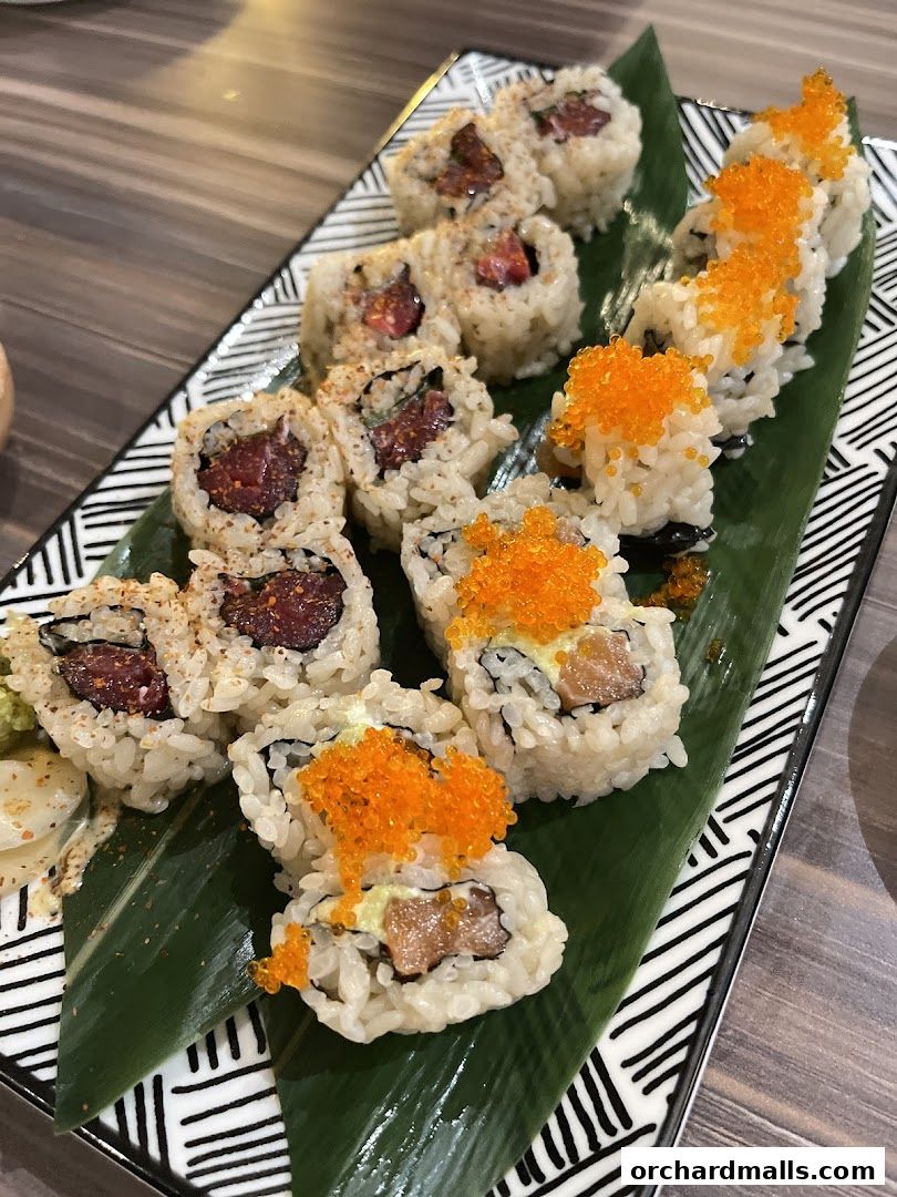 A platter of assorted sushi rolls, some topped with orange roe, served on a banana leaf.