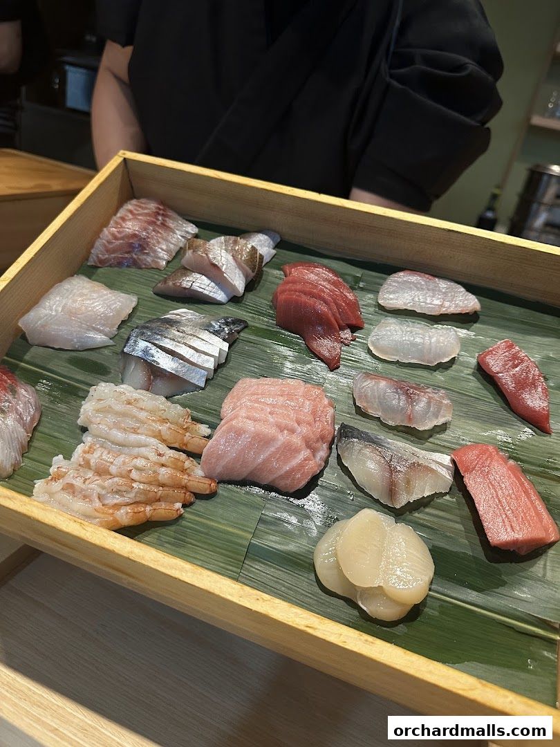 A wooden tray filled with assorted fresh sashimi and shrimp, prepared by a chef.