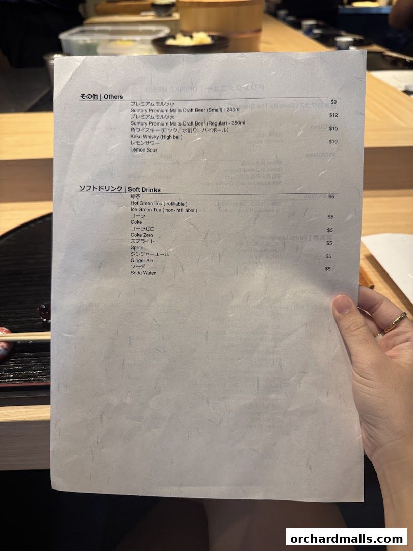 A hand holds a menu from Sushi Kyuu By Shunsui, listing drinks and prices.