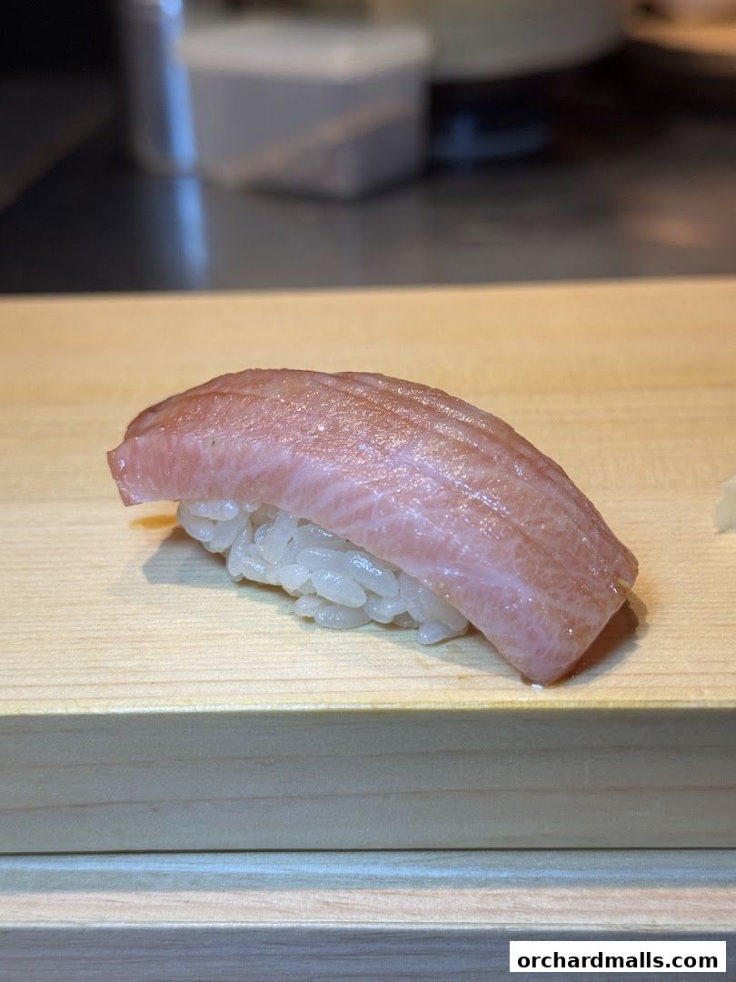 A close-up of a single piece of tuna nigiri sushi on a wooden board.