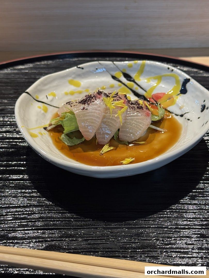 A beautifully presented dish of thinly sliced raw fish with sauce and garnishes.
