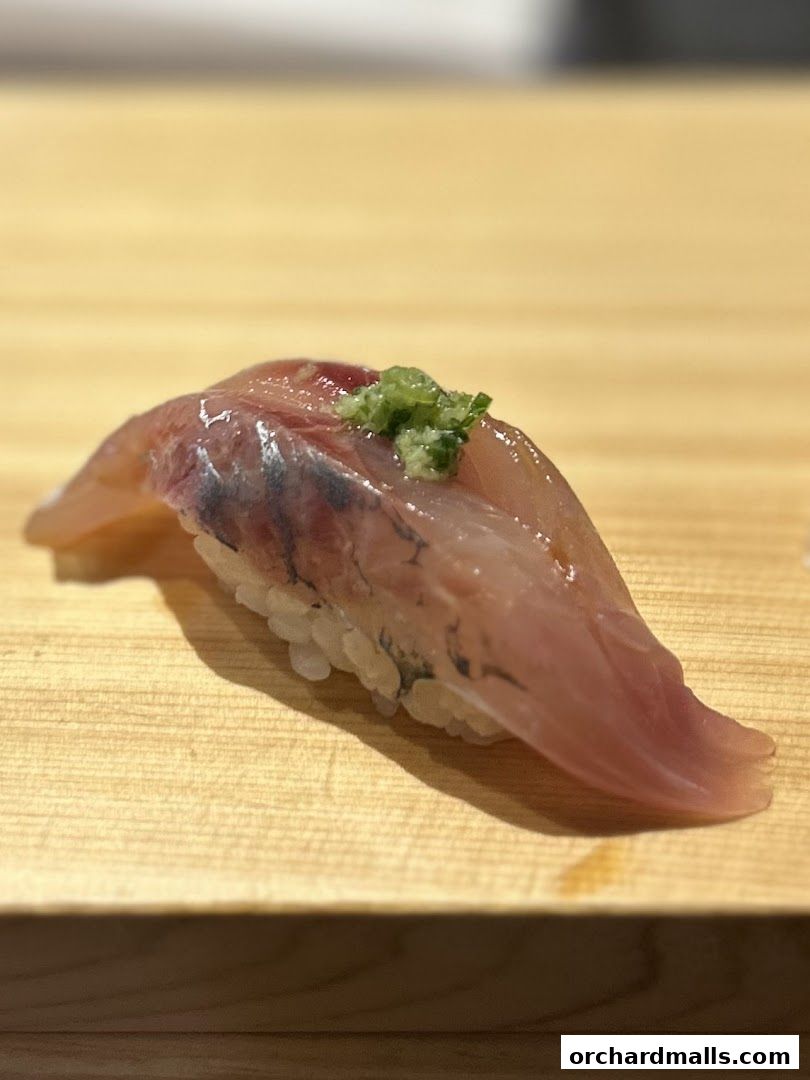 A close-up of a single piece of fresh sushi with raw fish and green garnish.