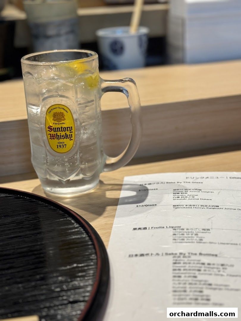 A glass of Suntory whisky highball with a lemon slice and a menu on a wooden counter.