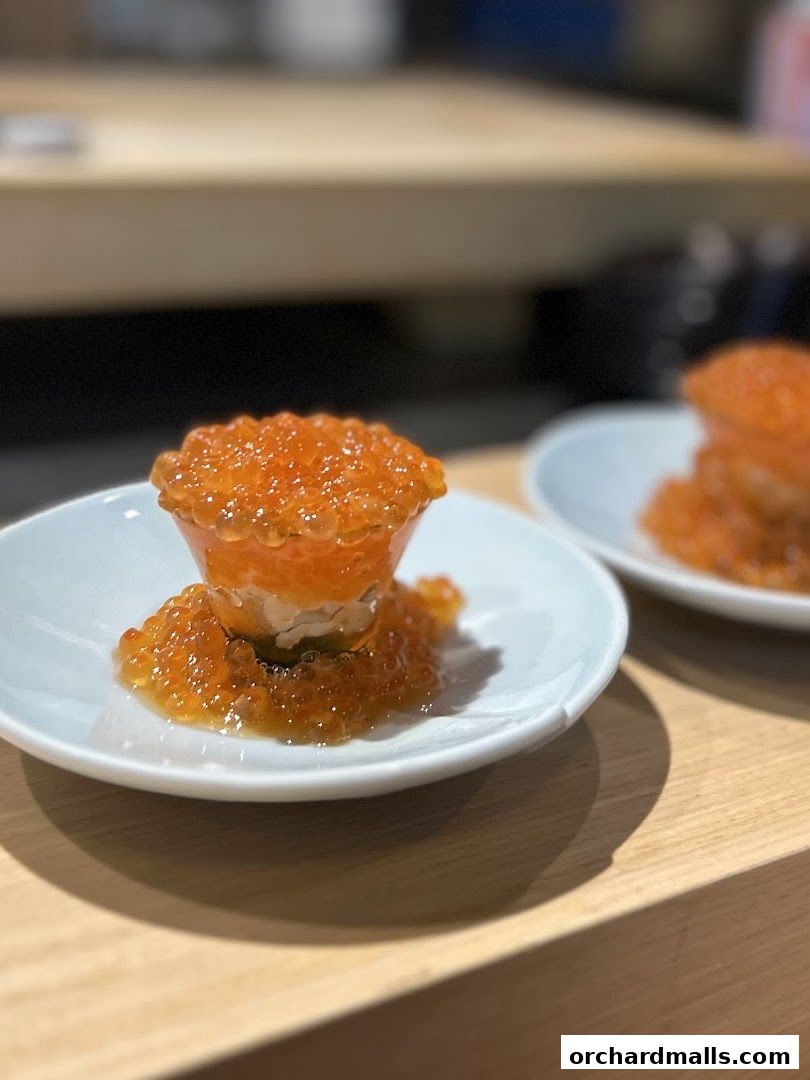 A close-up of a delicate sushi dish topped with vibrant orange ikura (salmon roe).