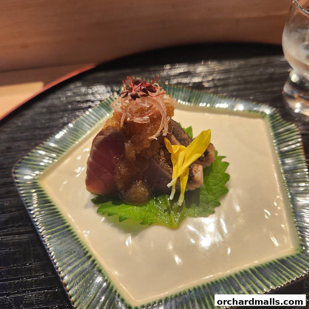 A beautifully plated dish of seared tuna with toppings and a yellow flower garnish.